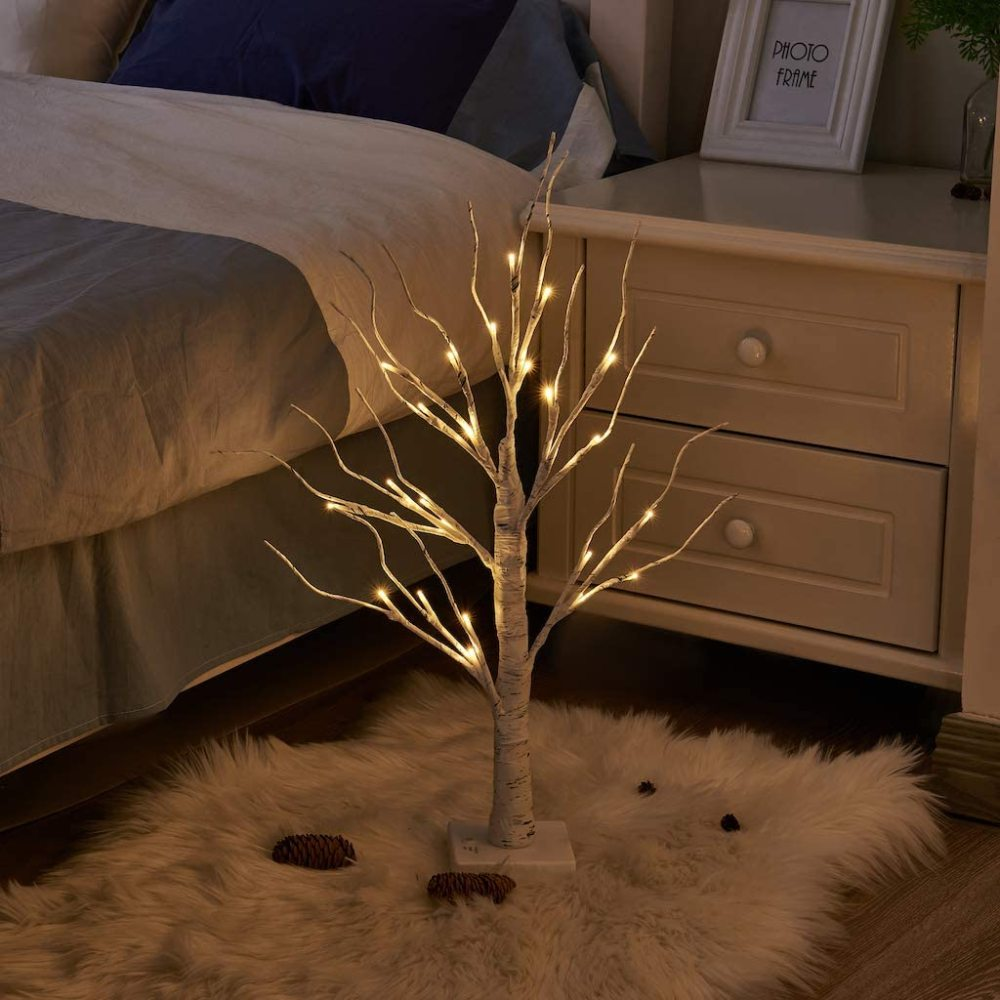 Ein beleuchteter Deko-Baum, im Hintergrund ein Bett und ein Nachttisch, auf einem weißen Teppich.