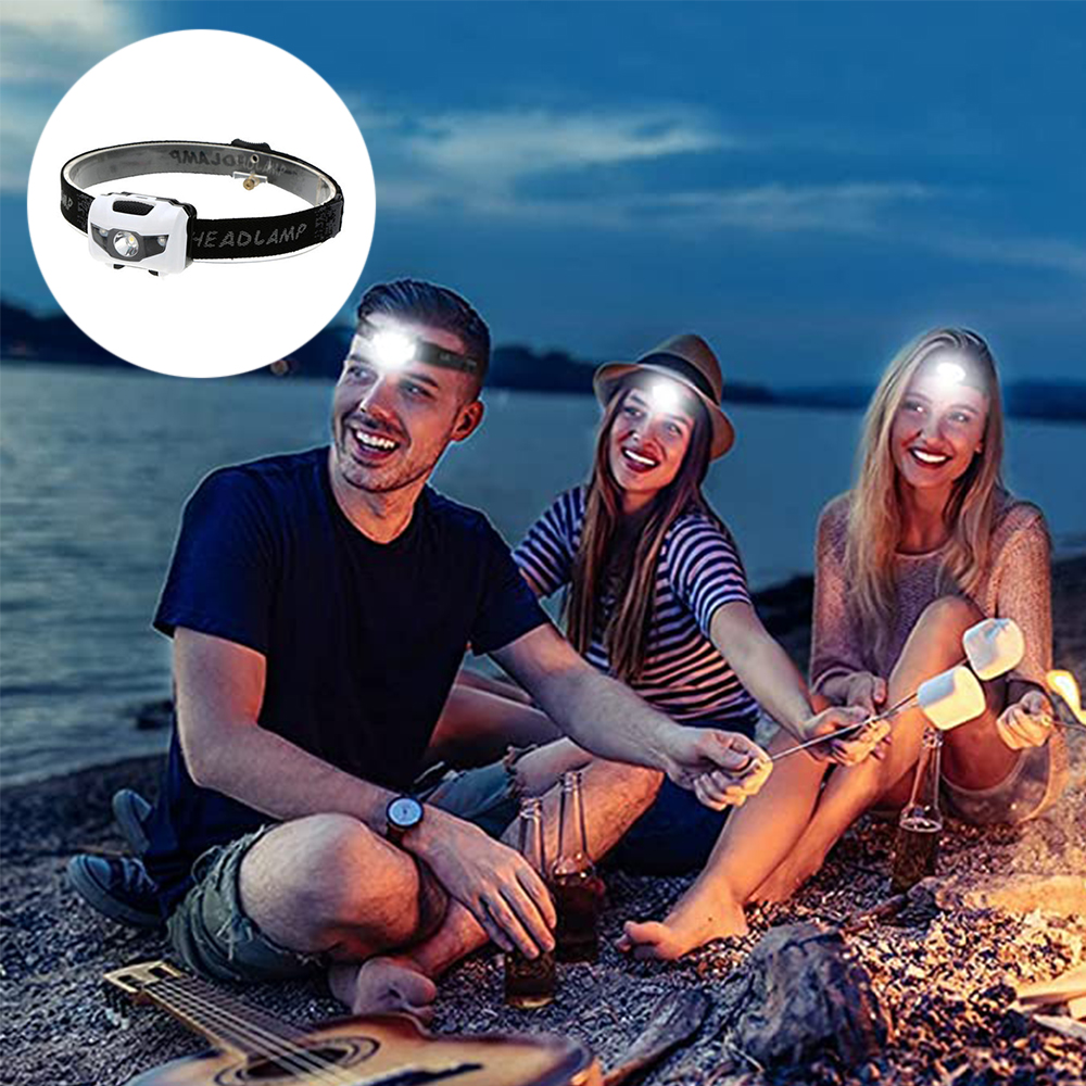 Drei Personen am Feuer mit Stirnlampen, mit Gitarre und Marshmallows am Spieß.