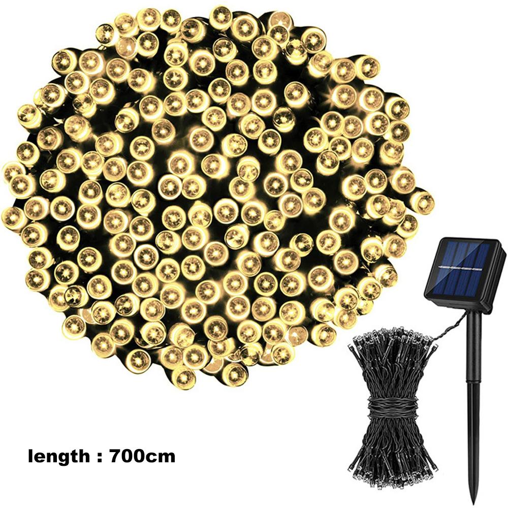 Solarbetriebene Lichterkette. Zahlreiche kleine Lichter an einem schwarzen Draht, ein Solarpanel und ein Pfahl.