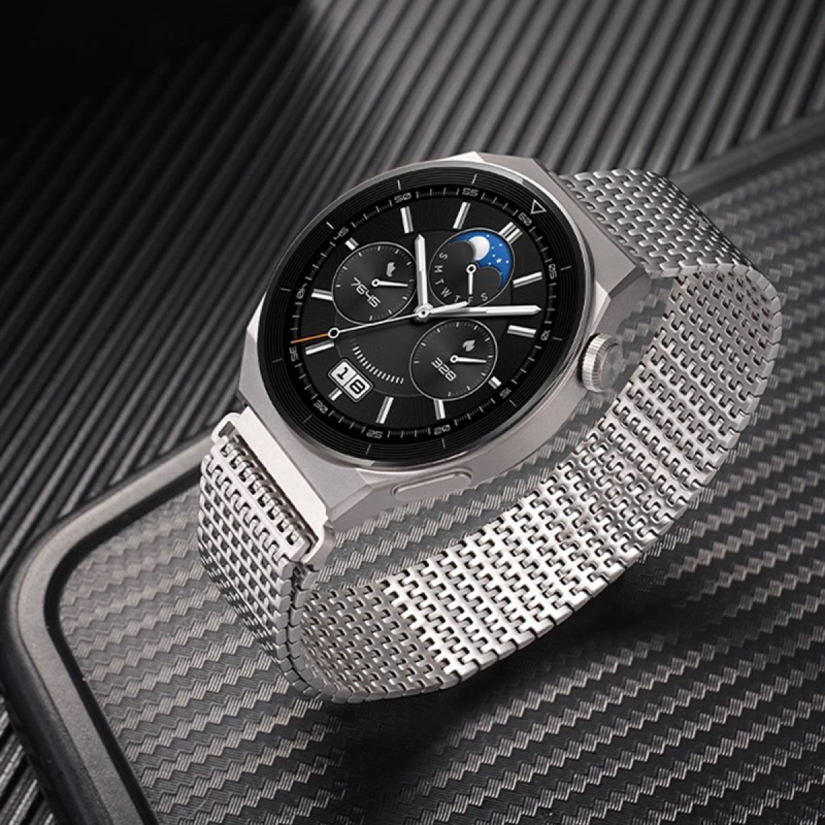 Silberne Smartwatch mit Mesh-Armband, zeigt Datum und Uhrzeit. Vor strukturiertem Hintergrund.