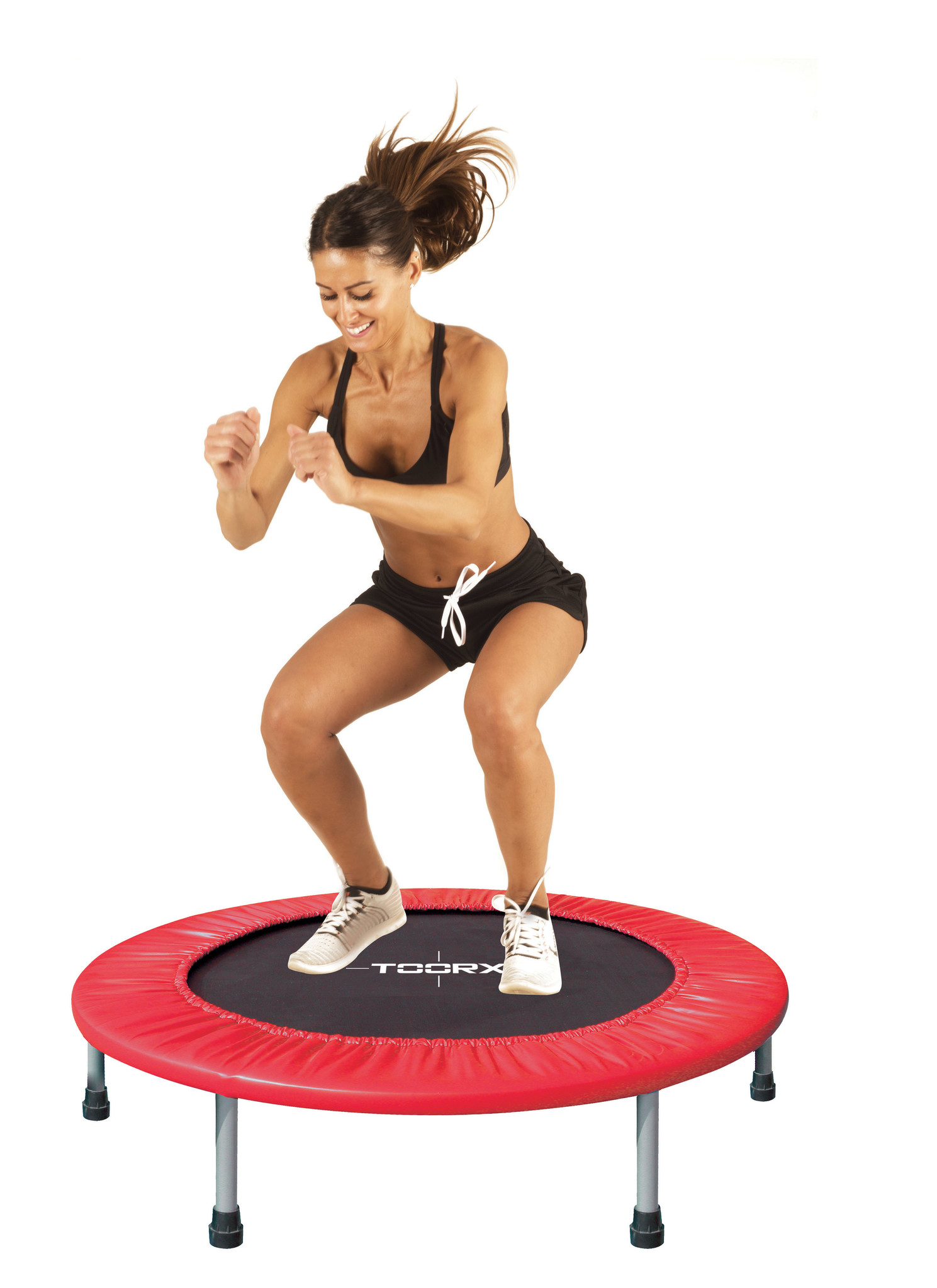 Eine Frau springt auf einem roten Trampolin. Sie trägt schwarze Shorts und einen Sport-BH.