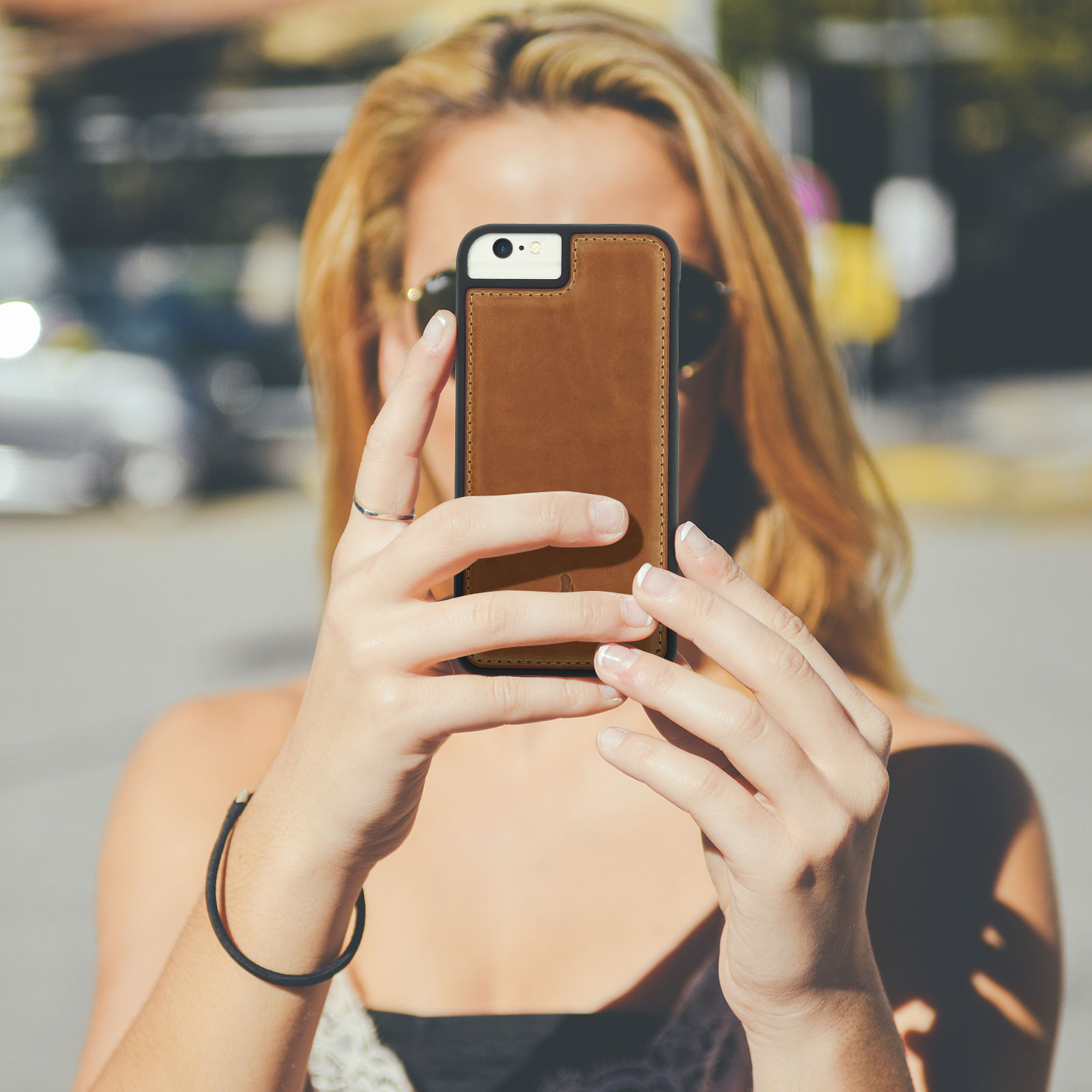 Donna che tiene in mano un telefono con custodia in pelle marrone, scattando una foto all'aperto al sole.