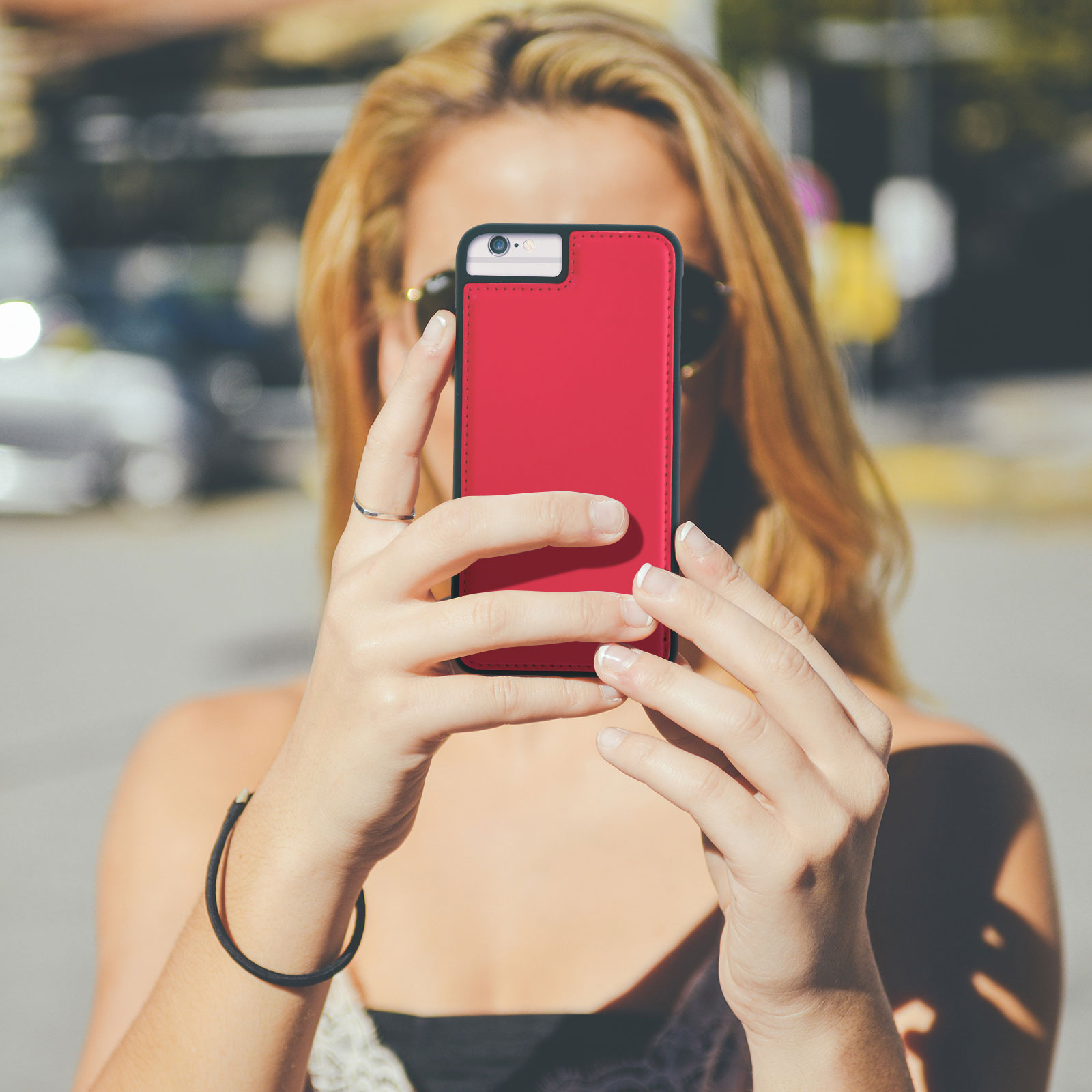 Donna che tiene una custodia rossa per telefono. Sta scattando una foto all'aperto. Giorno di sole.