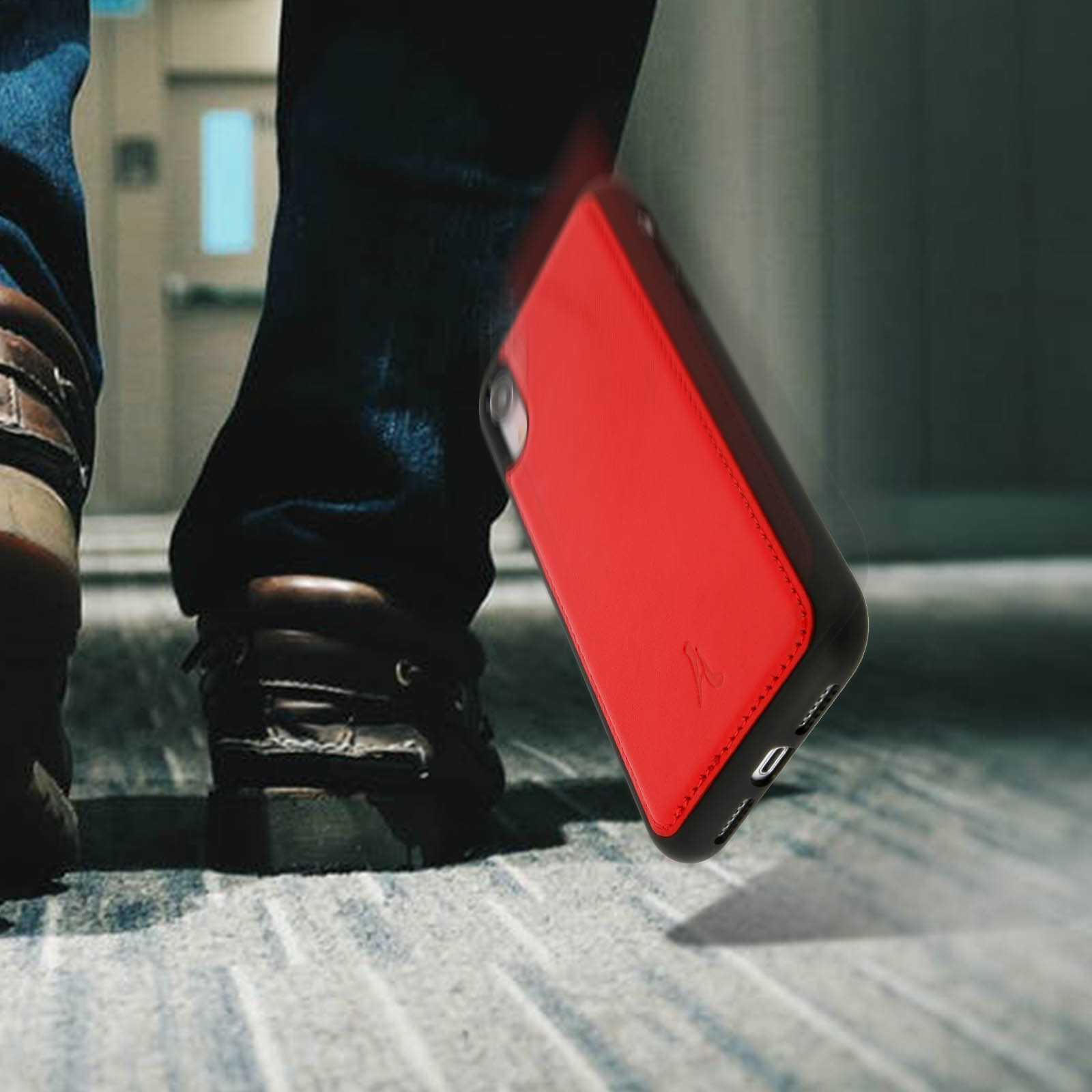 Gambe di una persona con custodia rossa per telefono che cade a terra. Scarpe marroni e jeans.