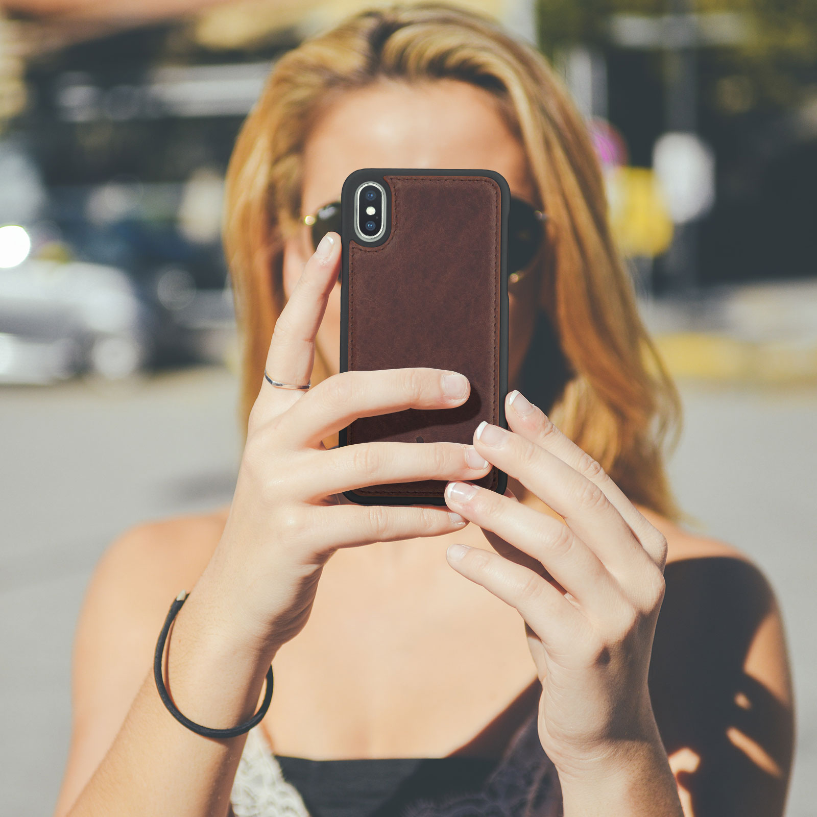Donna che tiene in mano un telefono, scatta una foto, sfondo sfocato, giornata di sole.