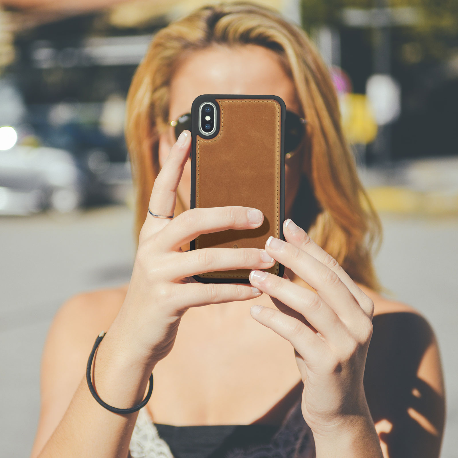 Donna che tiene un telefono, scatta una foto, con custodia in pelle marrone, al sole.