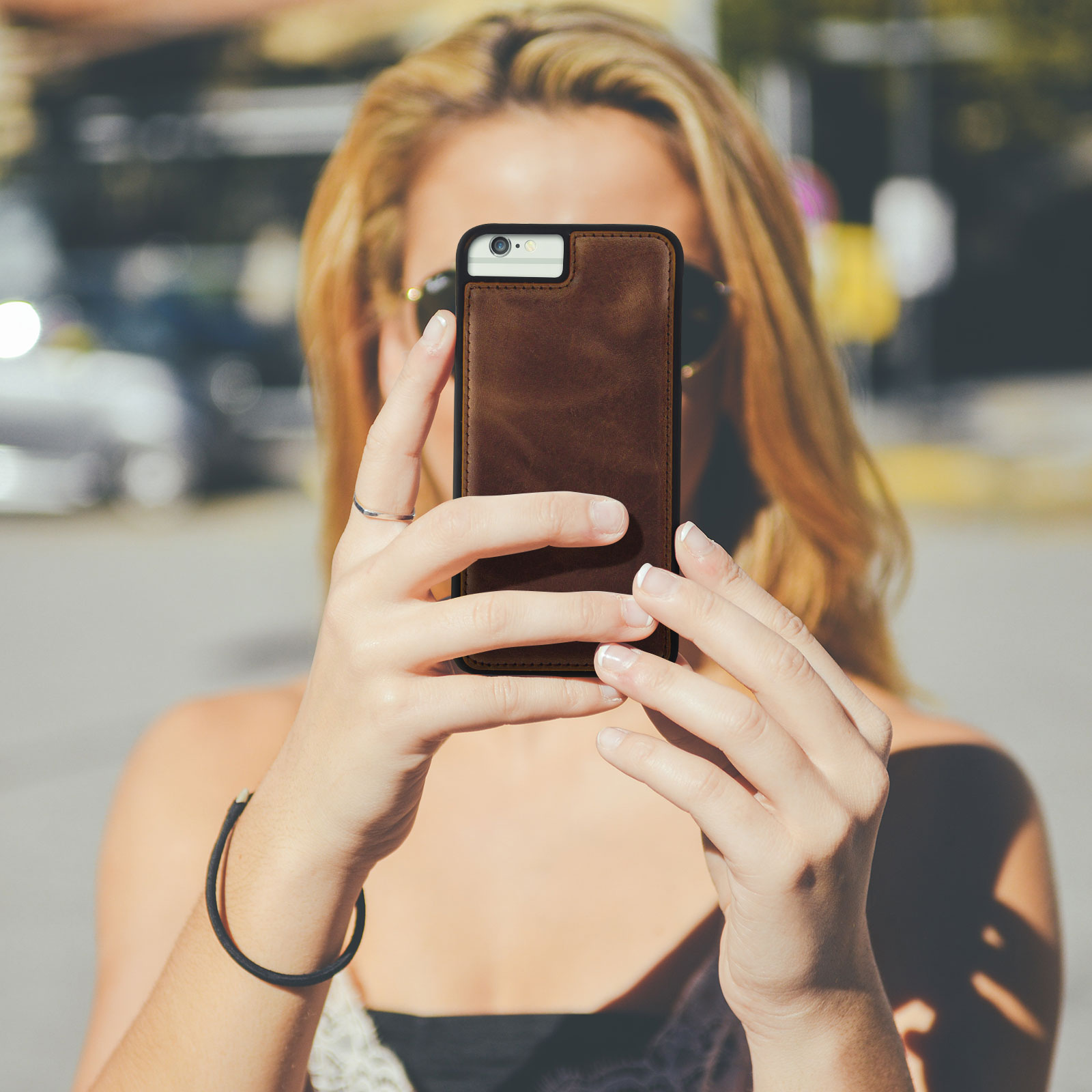 Una persona tiene in mano un telefono in una custodia di pelle marrone, scattando una foto, alla luce del sole.