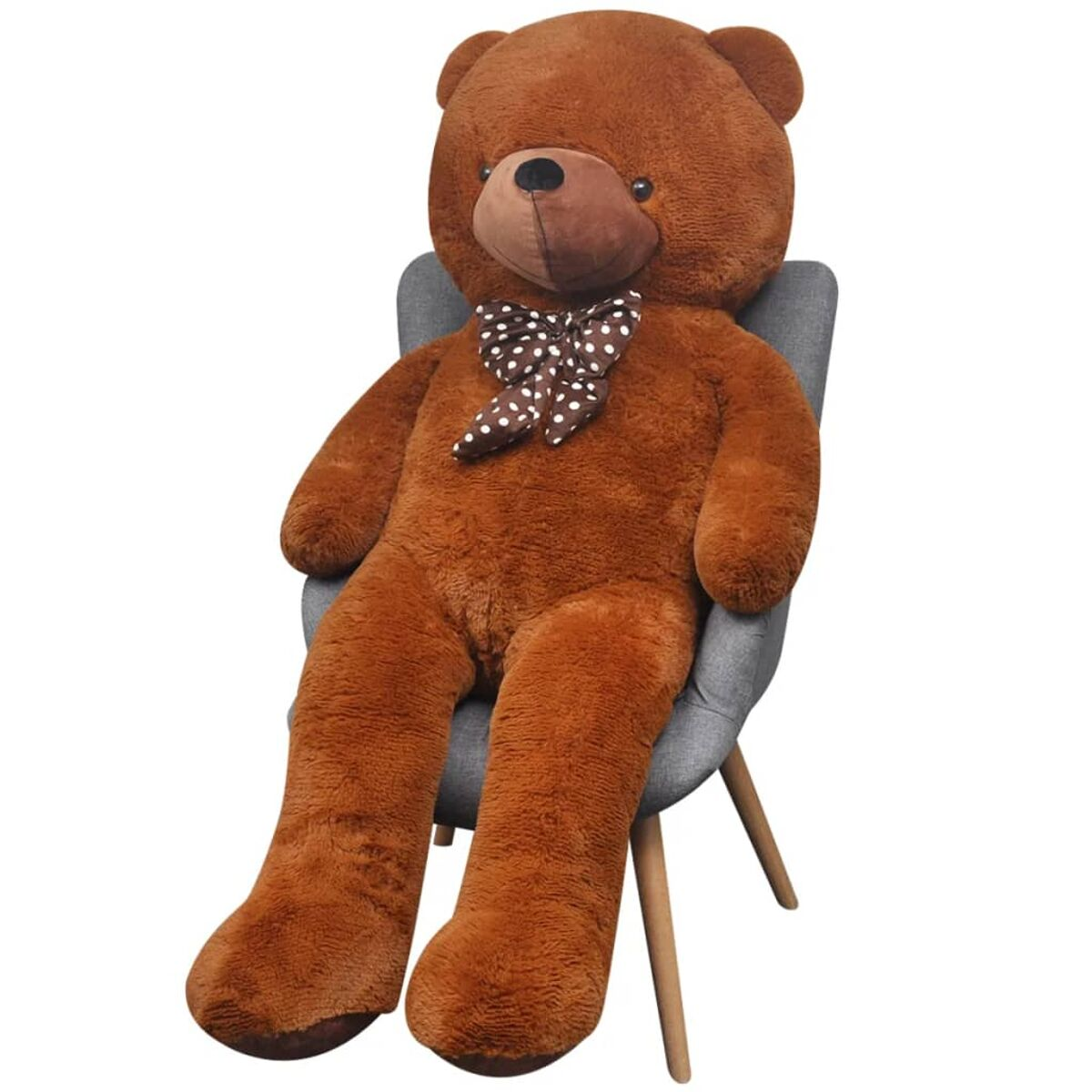 Ein großer brauner Teddybär mit gepunkteter Fliege sitzt auf einem grauen Stuhl vor weißem Hintergrund.