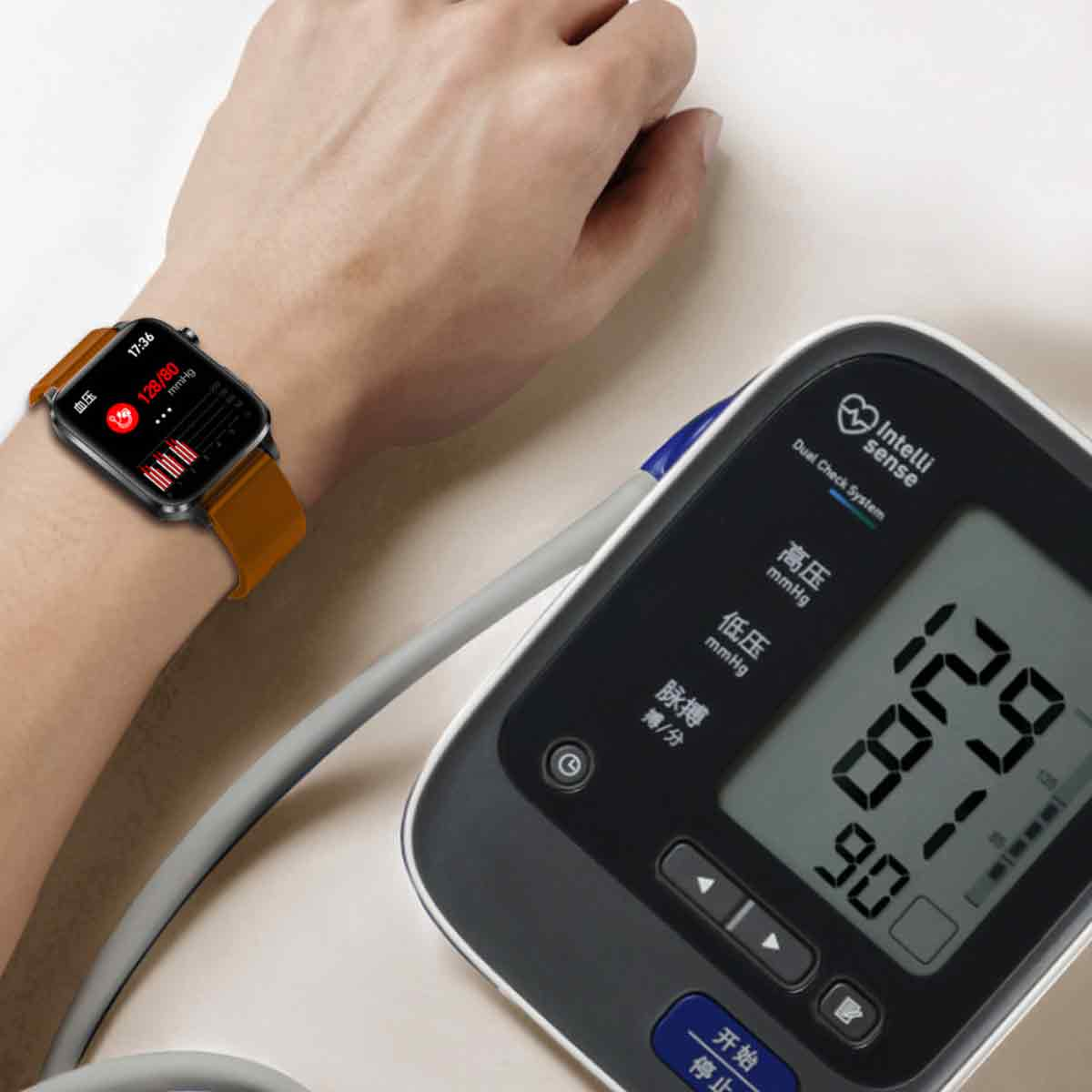 Das Handgelenk einer Person mit einer Smartwatch, die Blutdruckwerte anzeigt. Daneben ein Blutdruckmessgerät.