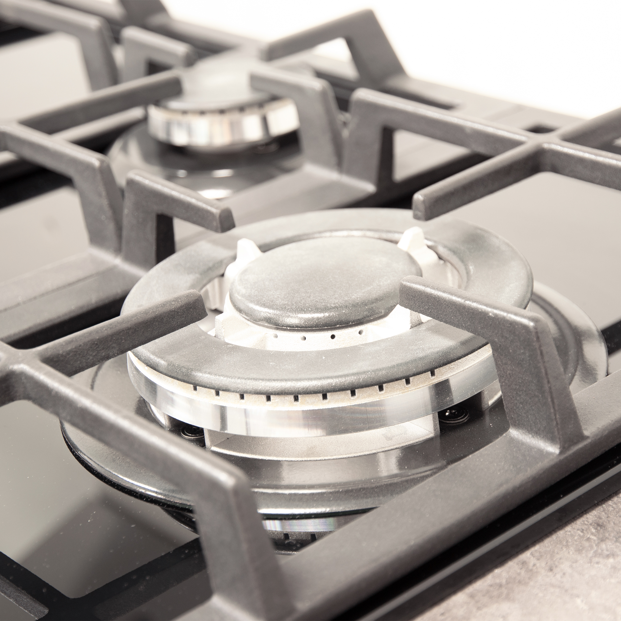 Zbliżenie palnika kuchenki gazowej. Ma czarny ruszt i metalowy pierścień palnika. Tło jest rozmyte.