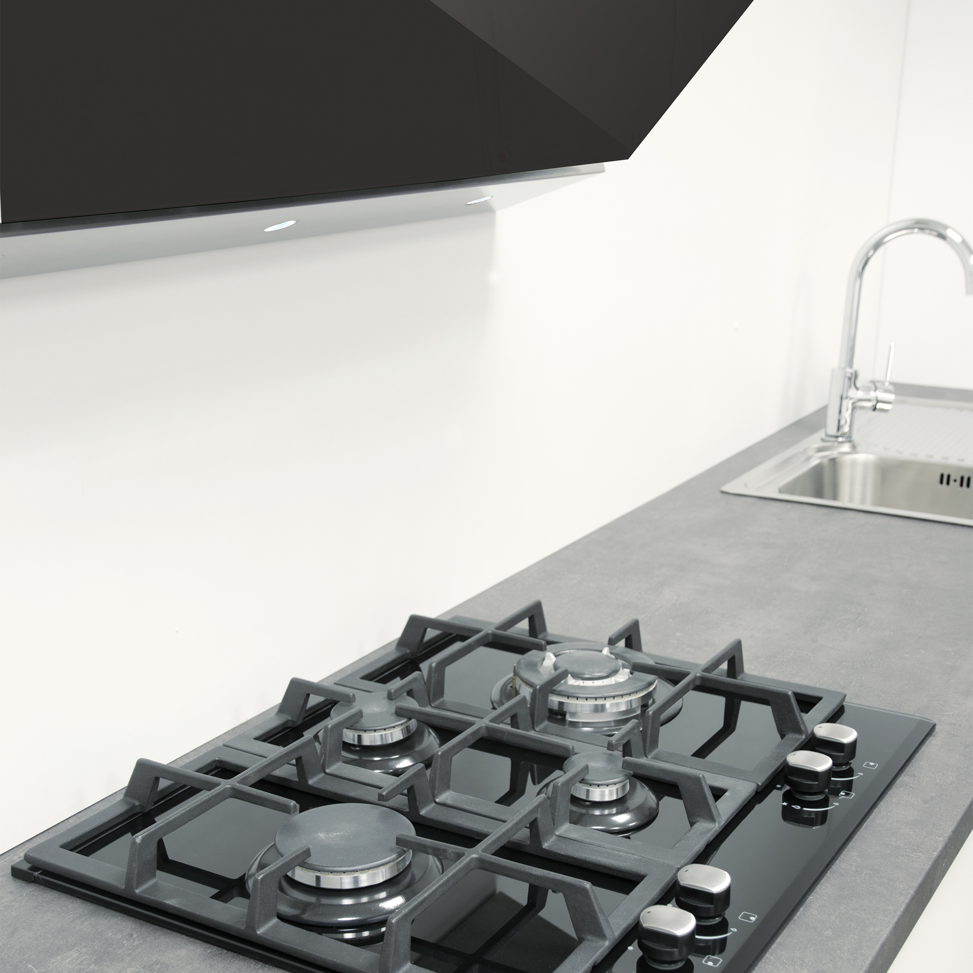 Scena kuchenna z czarną płytą grzejną, zlewem i białą ścianą. Czarny okap kuchenny wisi nad płytą.