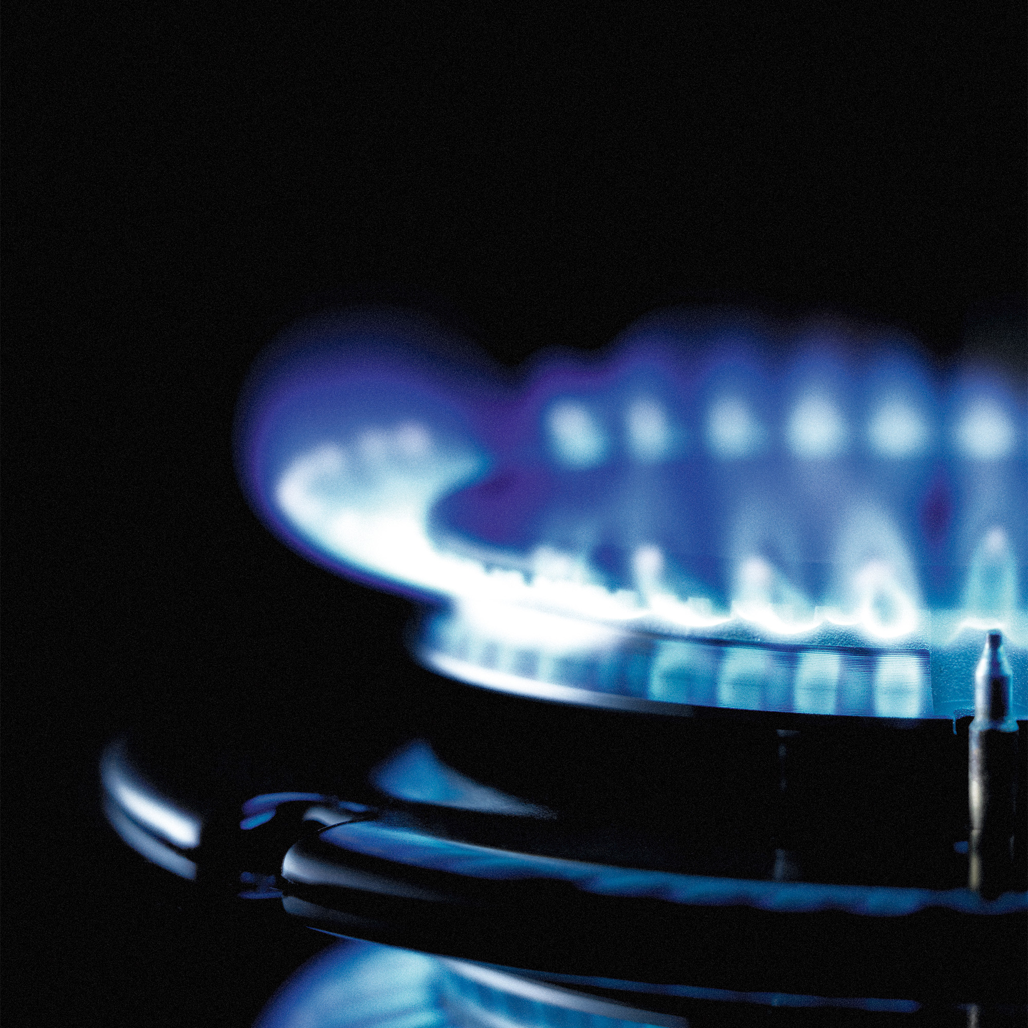 Primer plano de un quemador de gas con llamas azules sobre un fondo negro.