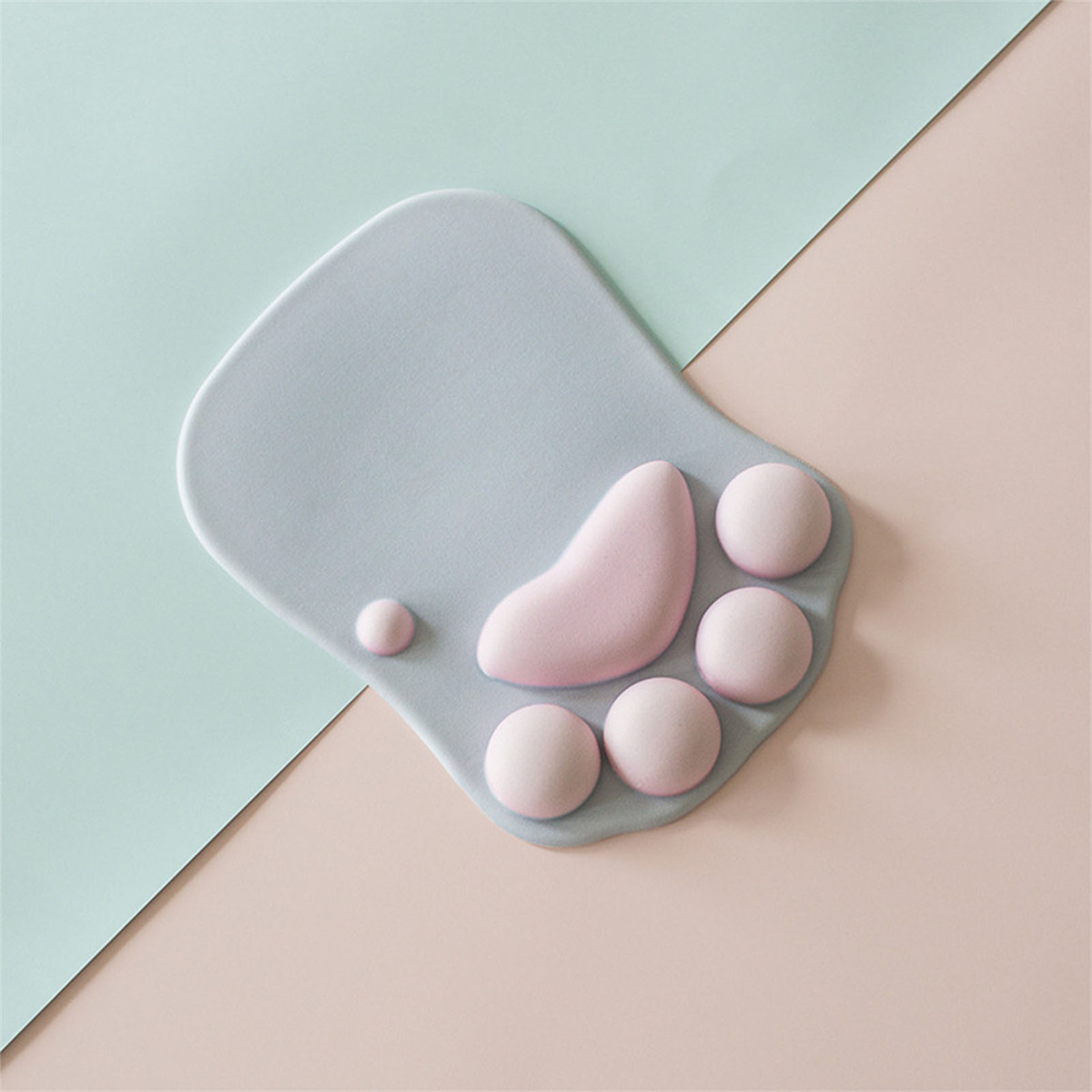 Ein mauspad in Katzenpfotenform, hellgrau mit rosa Pfotenpolstern. Der Hintergrund ist zwischen Türkis und Pfirsich geteilt.
