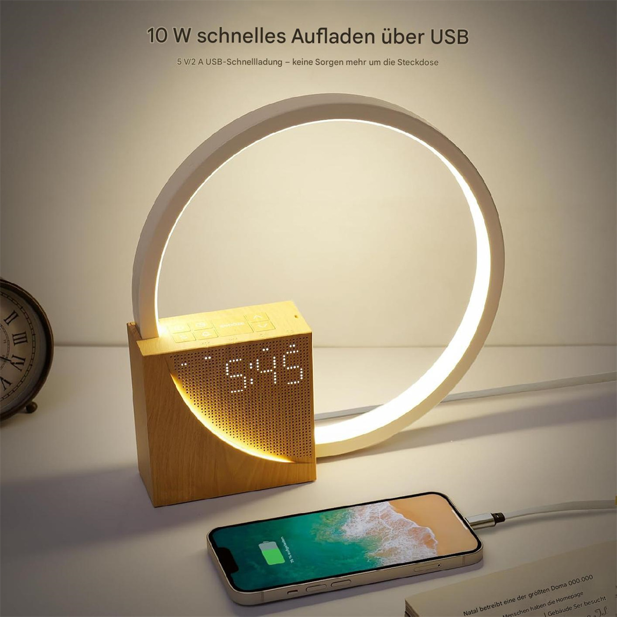 Eine hölzerne Schreibtischlampe mit Ringlicht und Digitaluhr. Ein Telefon wird auf dem Schreibtisch geladen.