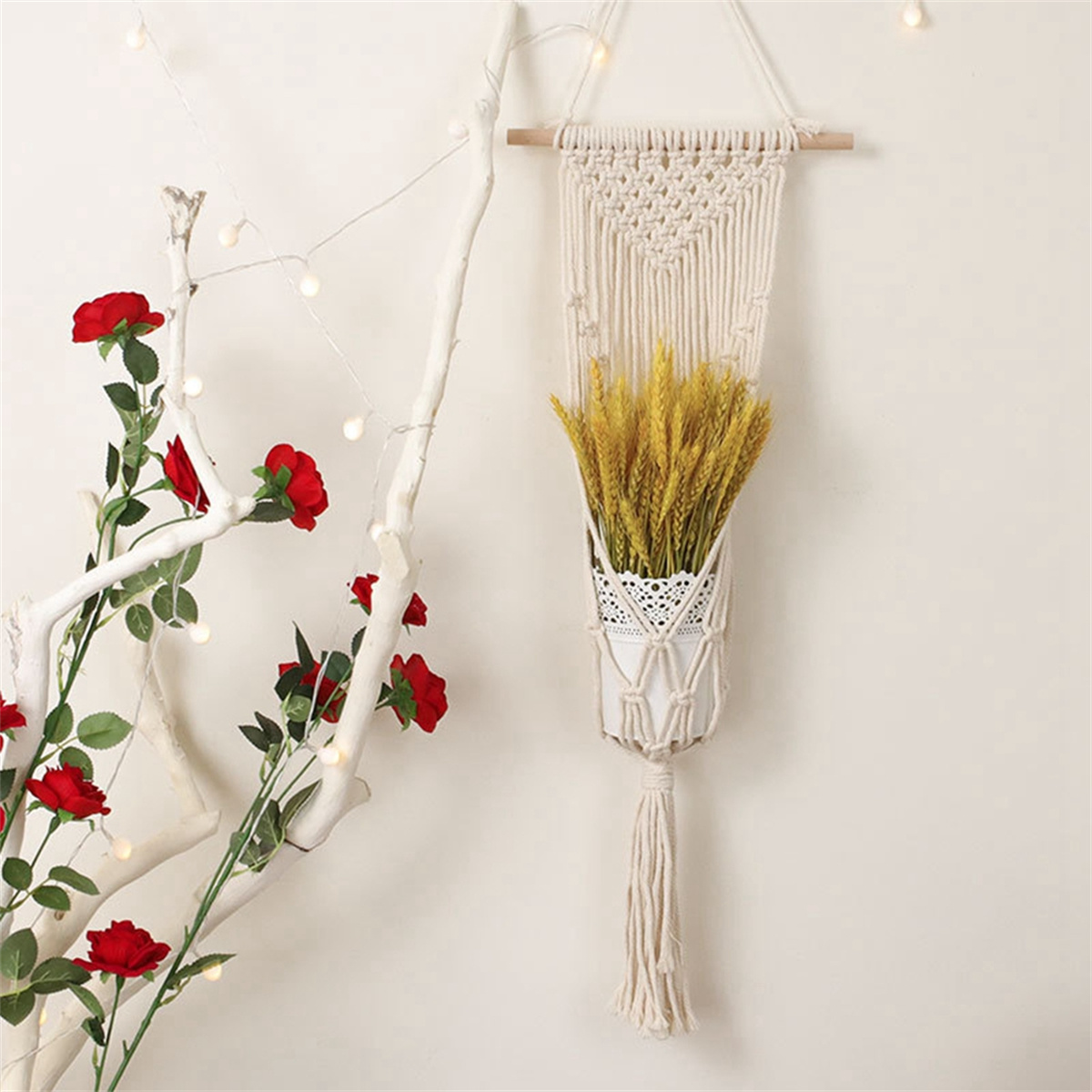 Eine gewebte Wanddekoration mit Weizen und roten Rosen. Weißer Hintergrund mit einem Ast und Lichtern.