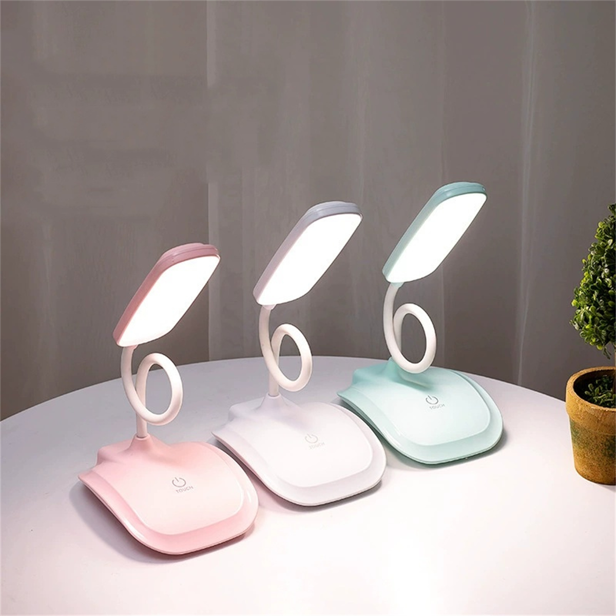 Drei Schreibtischlampen mit gebogenen Hälsen, in Rosa, Weiß und Grün, auf einer weißen Oberfläche.