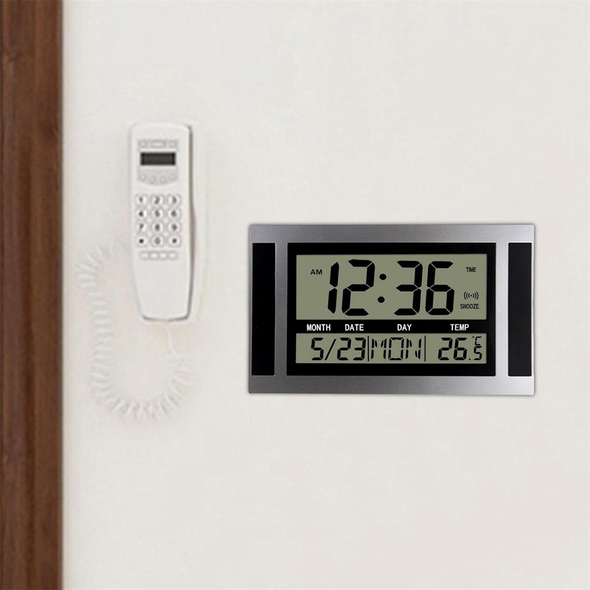 Digitaluhr und weißes Telefon an einer weißen Wand, mit Uhrzeit und Datum.
