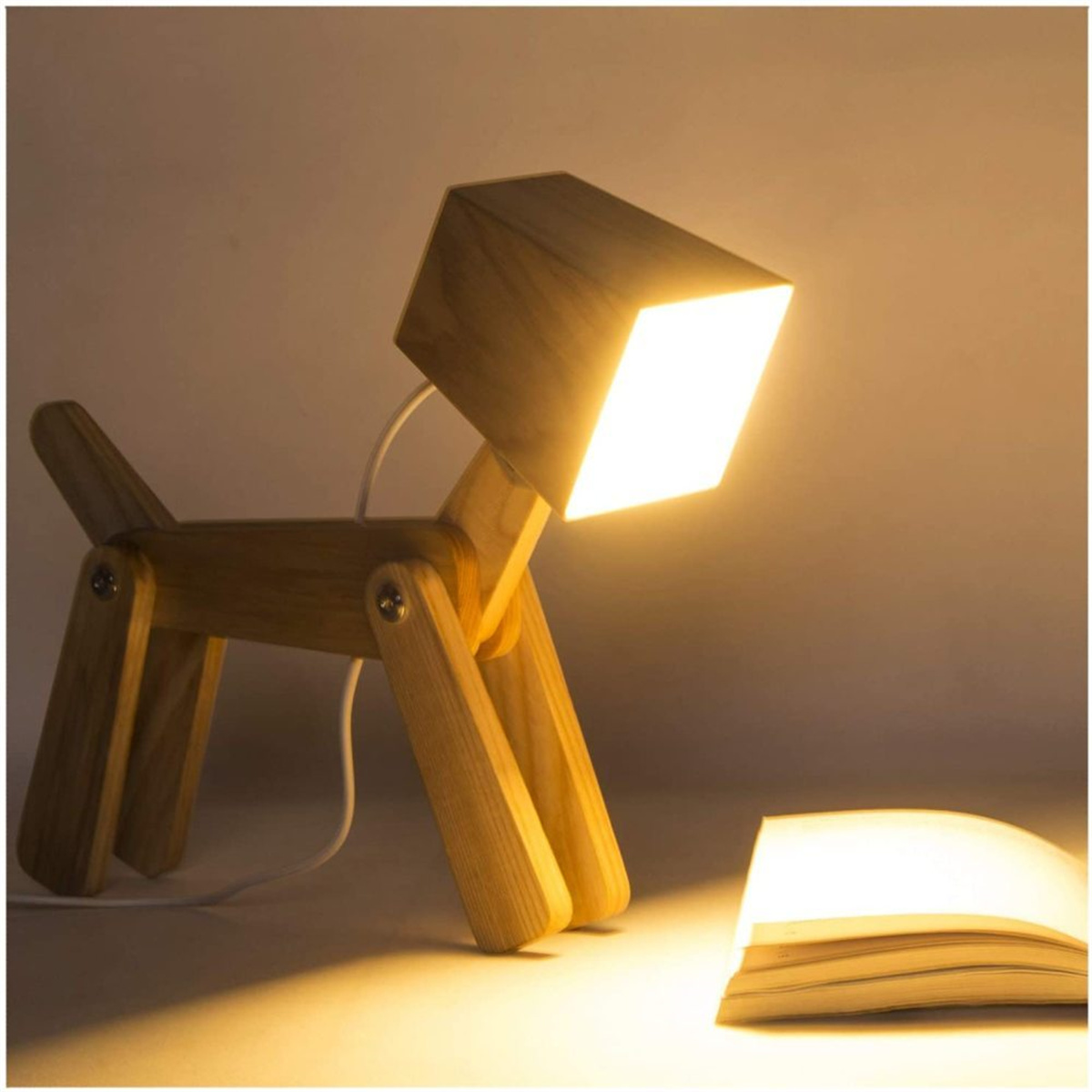 Holzlampe in Hundeform mit leuchtendem quadratischem Kopf, neben einem offenen Buch auf einem Schreibtisch.