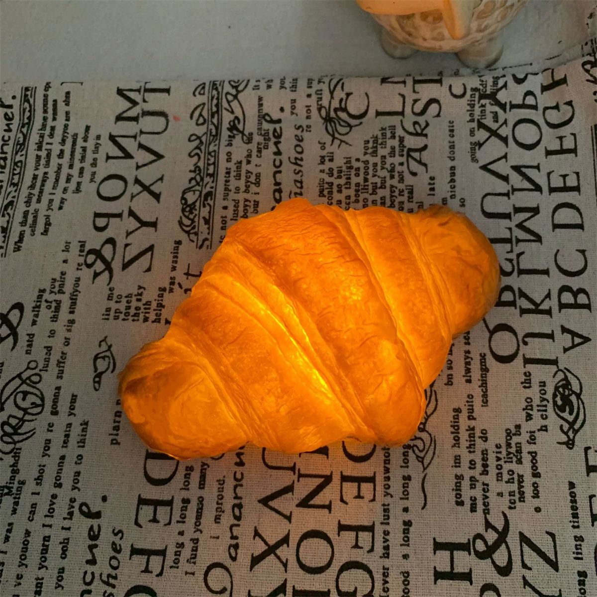 Ein beleuchtetes Croissant auf einem gemusterten Tuch. Der Hintergrund hat Text.
