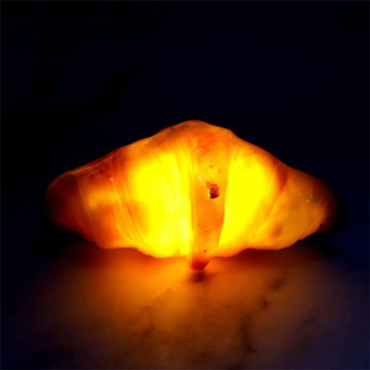 Ein glühendes Croissant. Das Gebäck ist von innen beleuchtet, wodurch ein warmer, einladender Effekt entsteht.