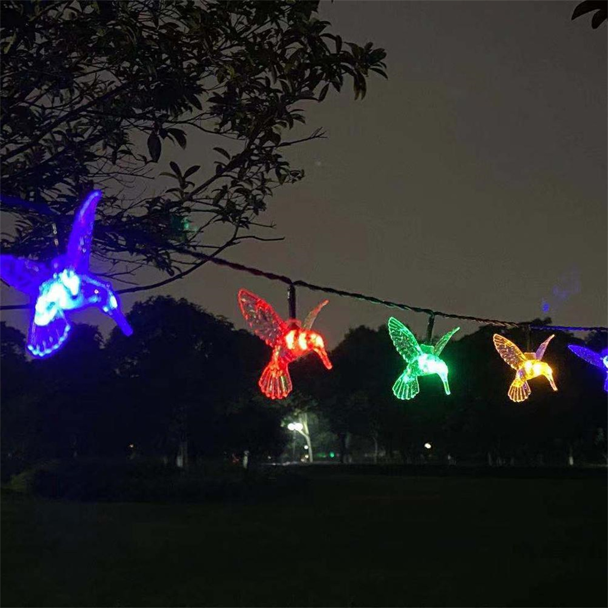 Lichterkette mit Kolibri-Dekorationen. Jeder Kolibri hat eine andere Farbe; draußen bei Dämmerung.