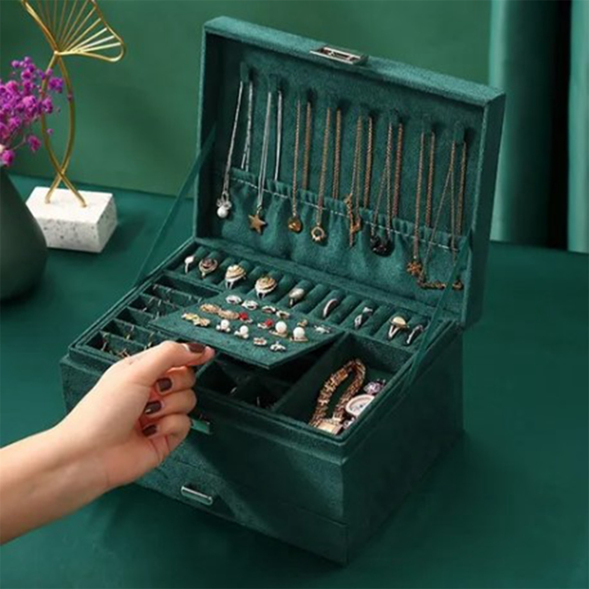 Offene grüne Schmuckschatulle mit Halsketten, Ringen und Armbändern.