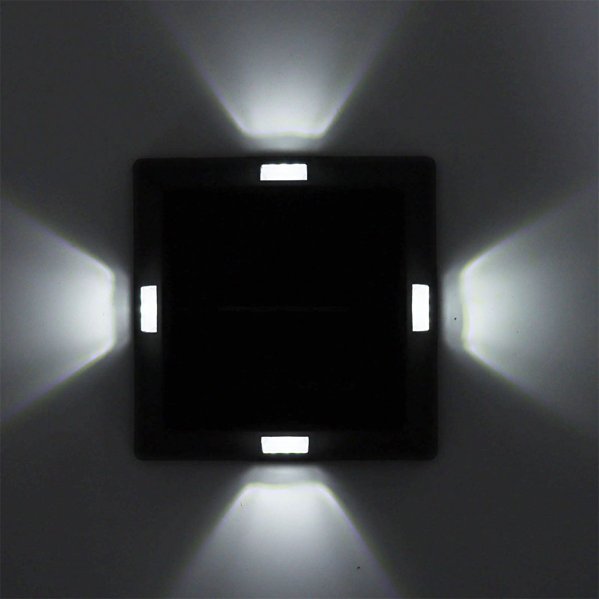 Quadratische schwarze Wandleuchte mit vier Lichtstrahlen. Die Lichtstrahlen sind nach außen gerichtet.