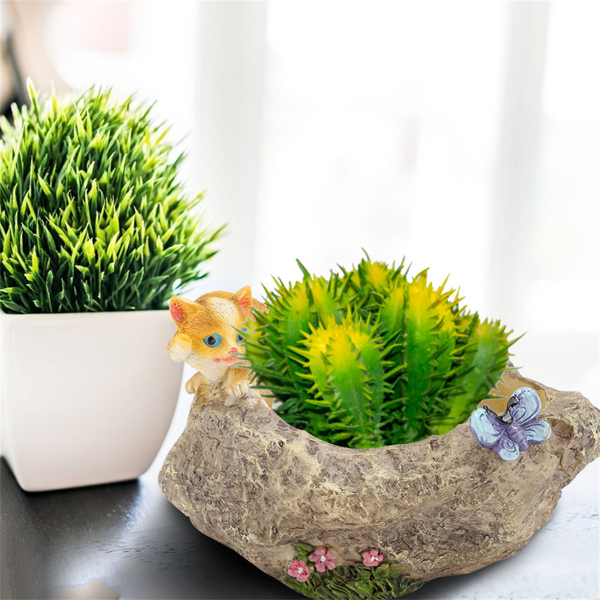 Zwei Pflanzen in Töpfen. Einer ist ein katzenförmiger Topf mit Kaktus und Schmetterling.
