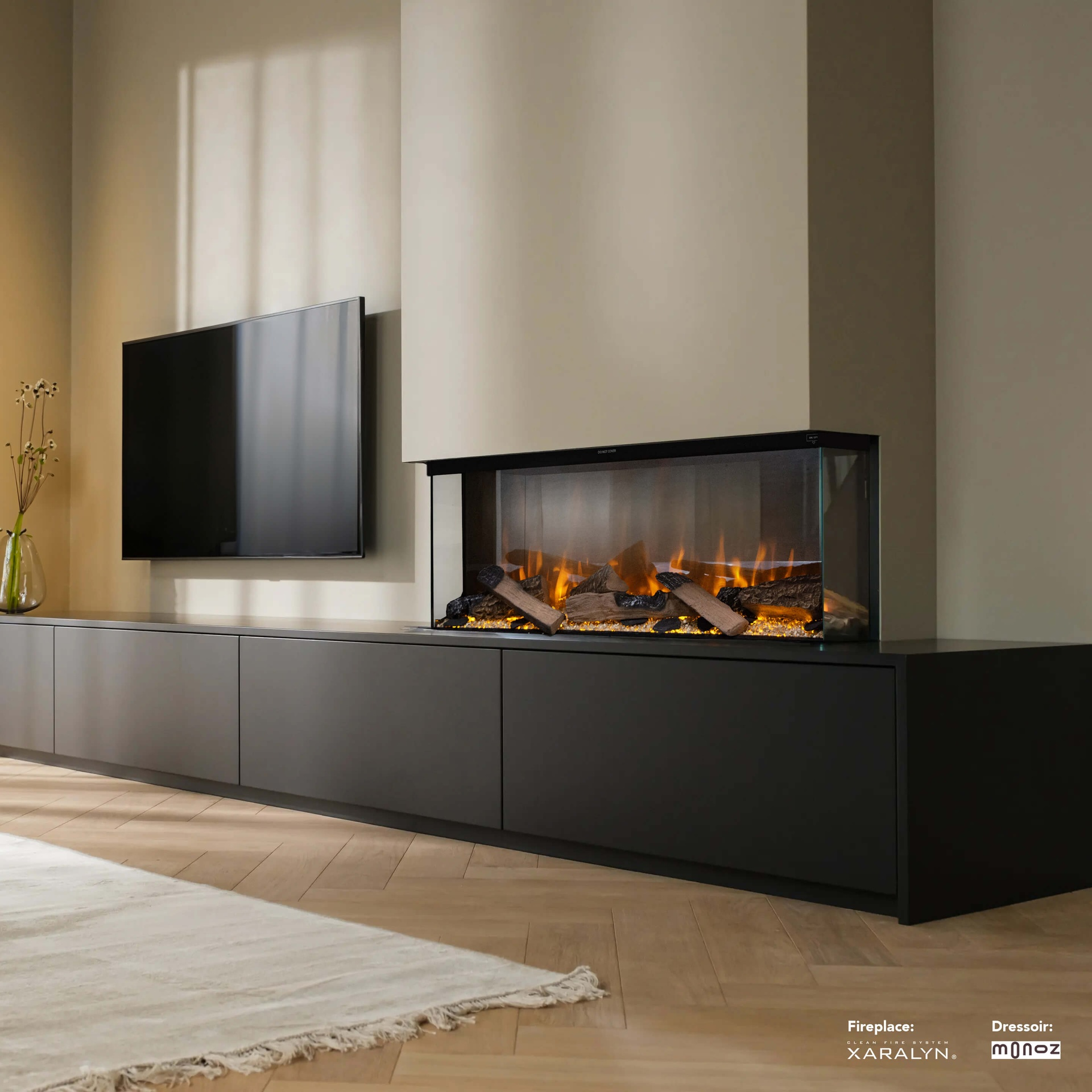 Een woonkamer met een zwarte tv, een open haard met vlammen en een zwarte kast. Er ligt een tapijt op de houten vloer.