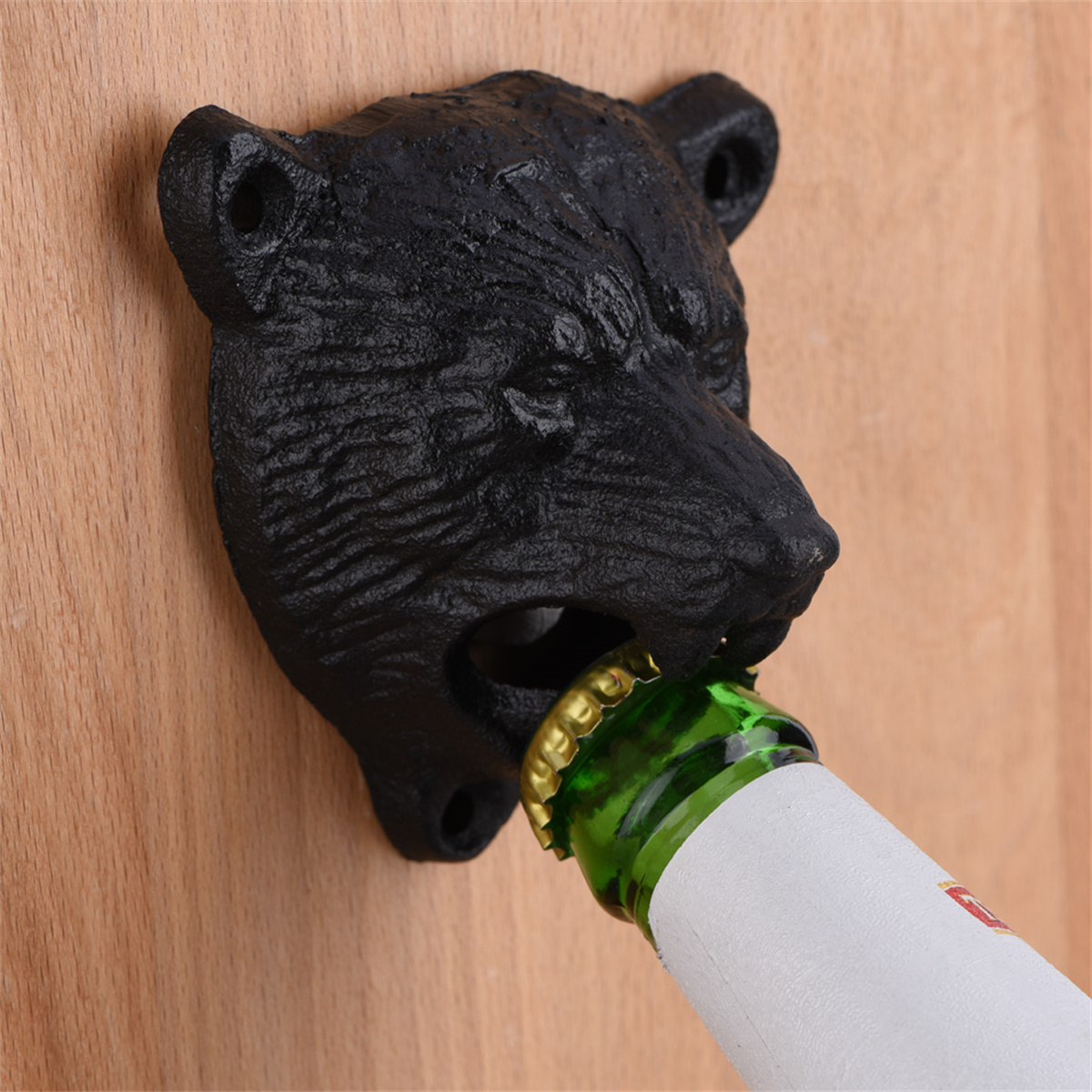 Schwarzer Bärenkopf-Flaschenöffner an Holz montiert. Eine grüne Flasche wird geöffnet, goldener Verschluss sichtbar.