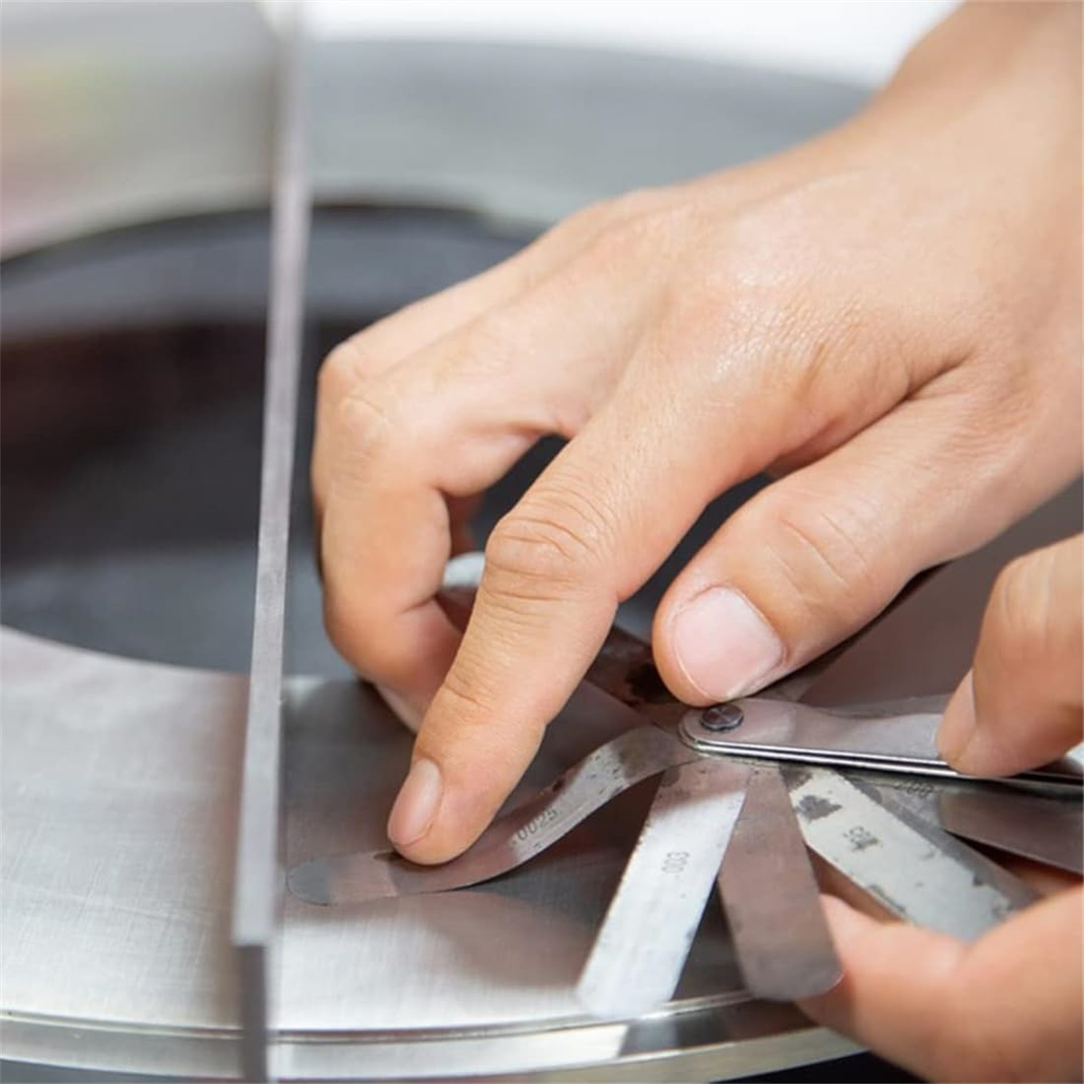Hände einer Person, die eine Fühlerlehre verwenden, um den Spalt zwischen zwei Metallplatten zu messen.