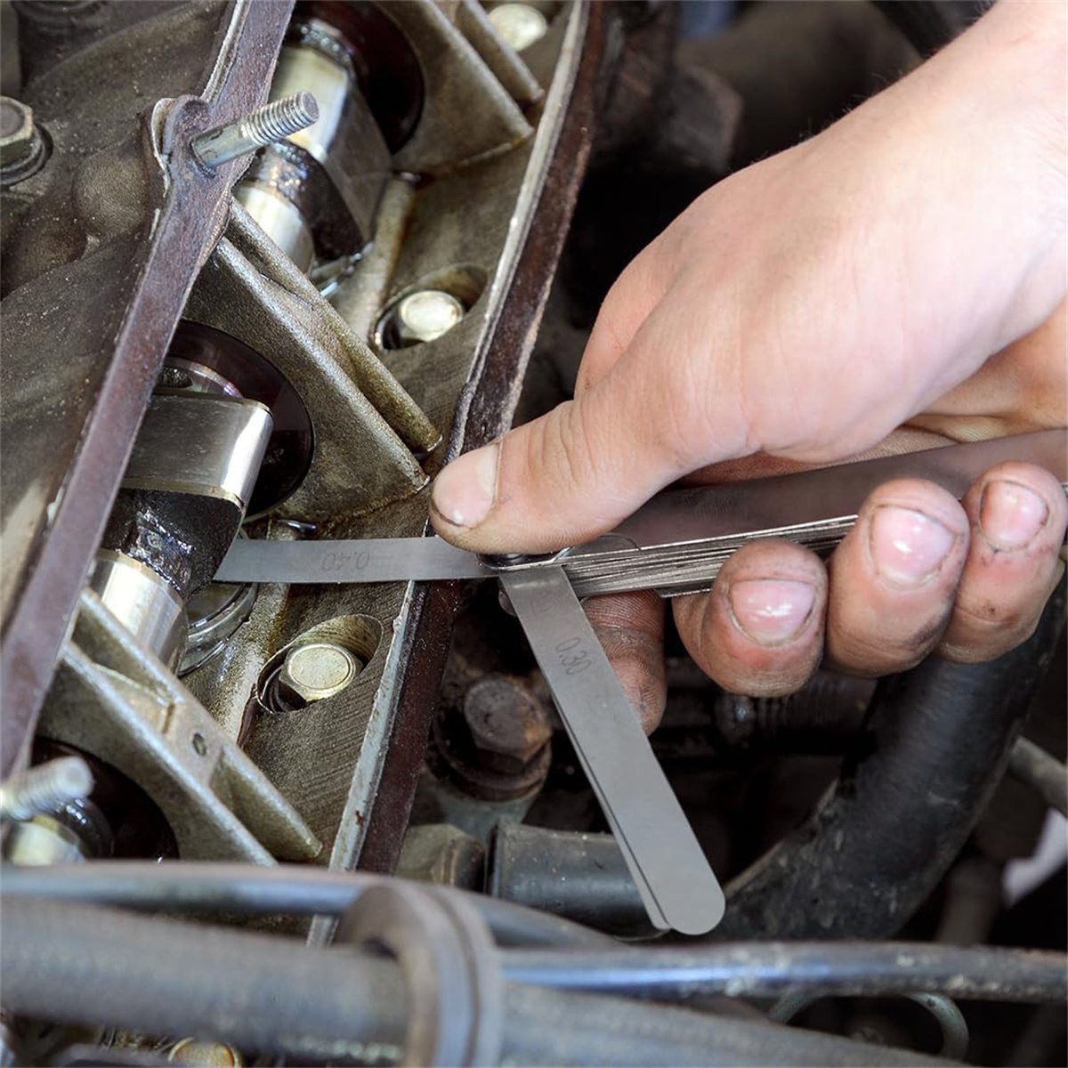 Hand verwendet eine Fühlerlehre an einem Motor. Der Motor ist teilweise sichtbar.