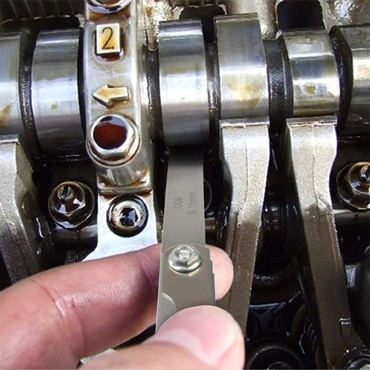 Die Hand einer Person misst mit einer Fühlerlehre den Spalt zwischen Motorkomponenten.