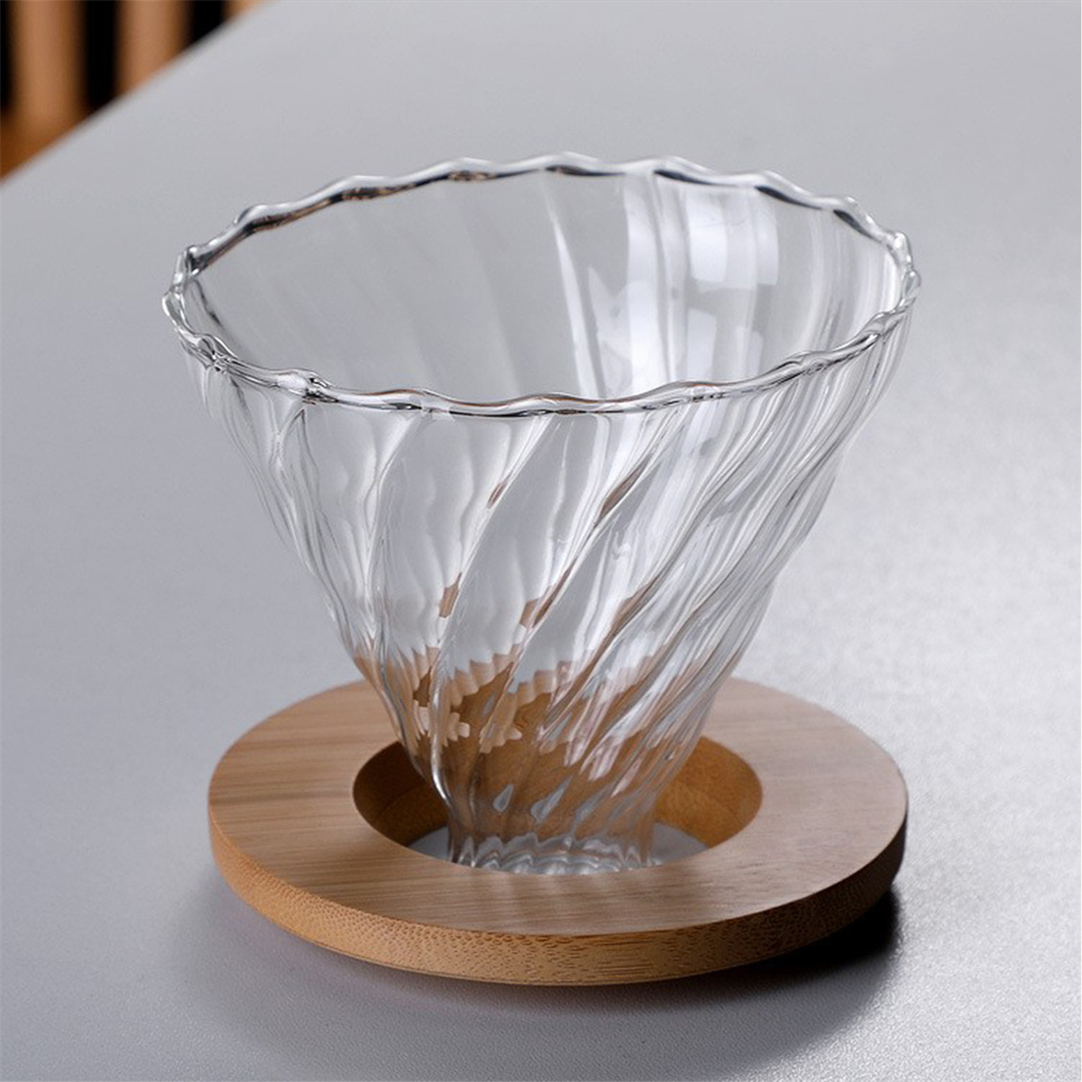 Klarer Glas-Kaffeetropfer auf Holzsockel, auf grauer Oberfläche.