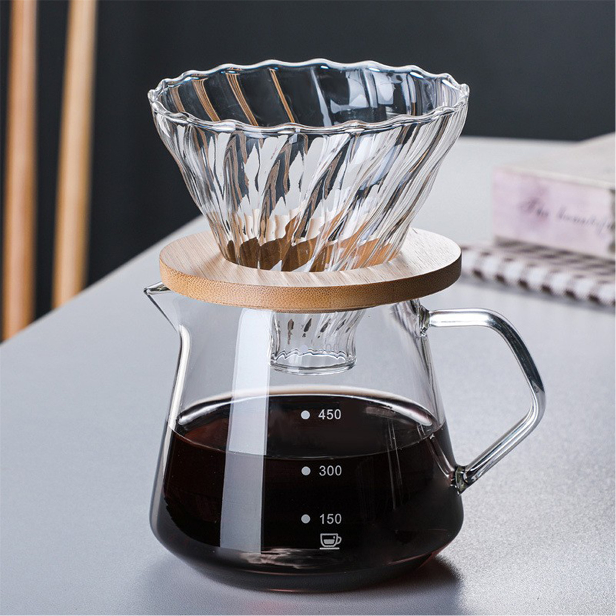 Ein Kaffeezubereiter aus Glas mit einem Holzring auf einer Karaffe mit dunklem Kaffee.