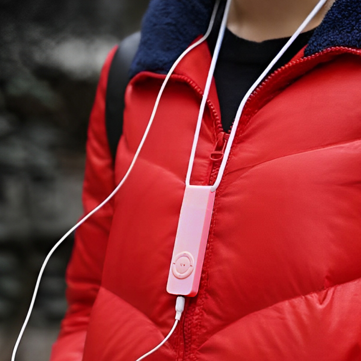 Eine Person mit roter Jacke hat ein rosa Gerät mit weißen Ohrhörern um den Hals hängen.