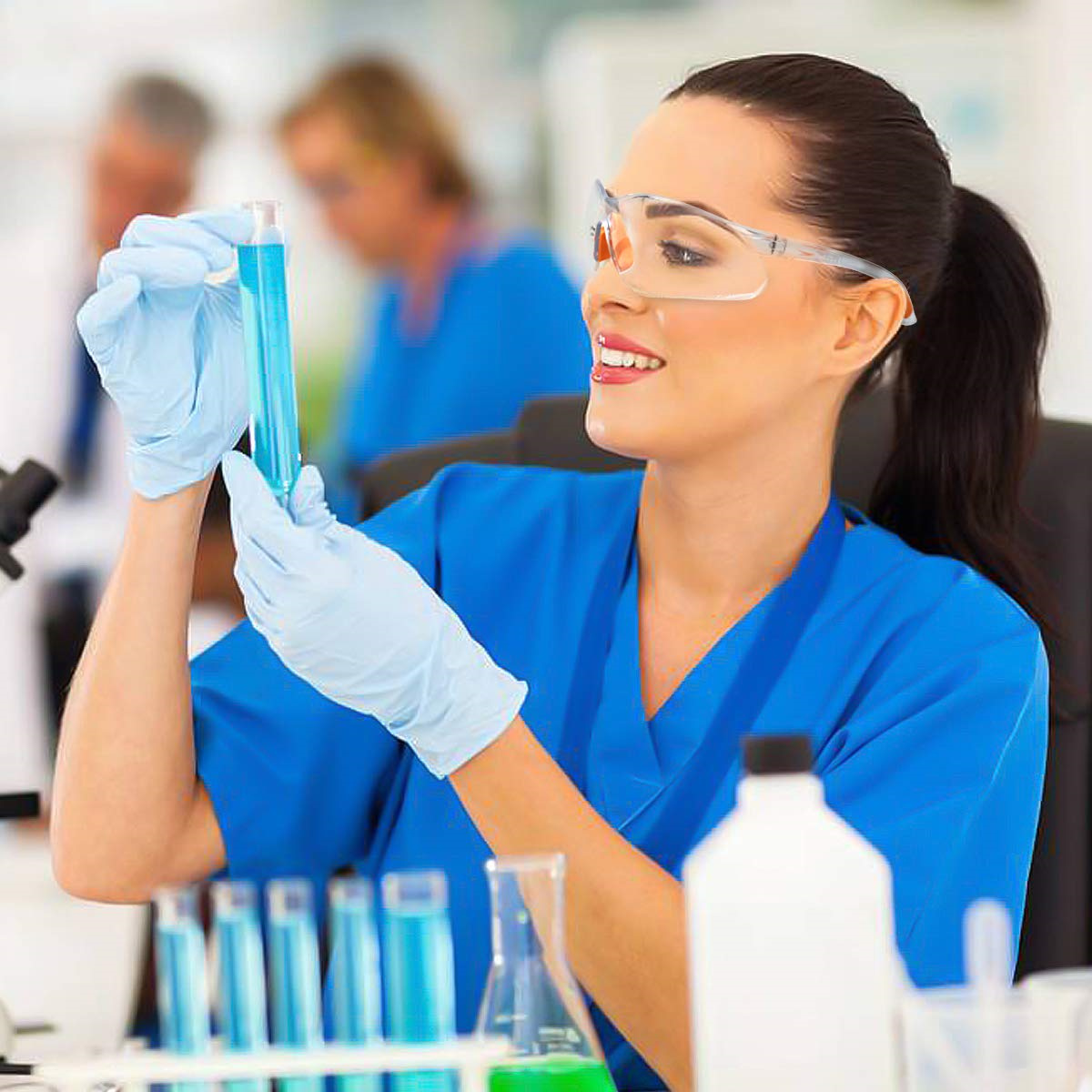 Wissenschaftlerin hält blaue Flüssigkeit in einem Reagenzglas, lächelt, in einem Labor.
