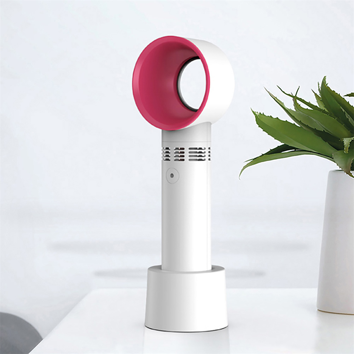 Weiß-rosa, blattloser Ventilator, zylindrischer Sockel, rosa Oberteil, auf weißem Tisch.