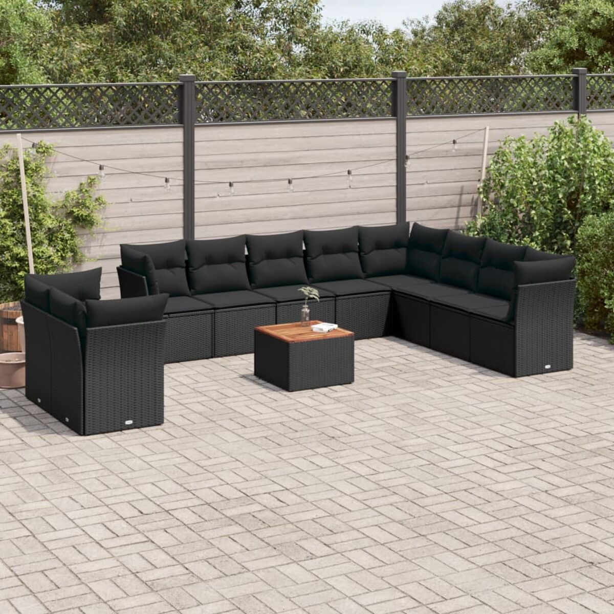 Set di mobili da esterno in rattan nero con cuscini, disposti su un patio con una recinzione in legno.
