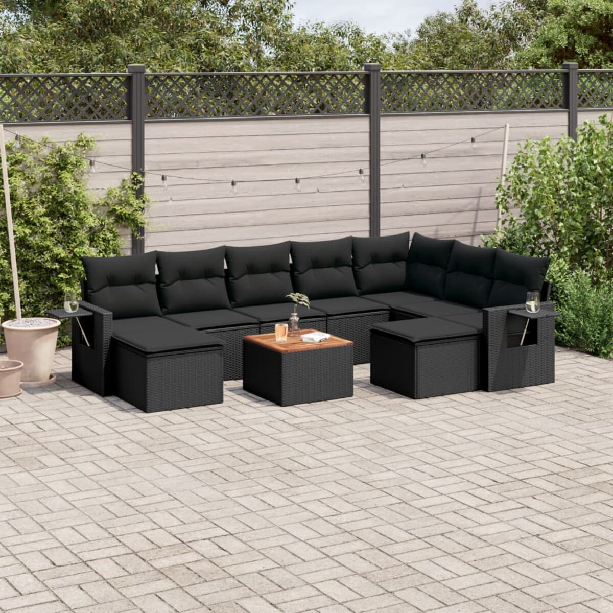 Set divani in rattan nero da esterno con tavolino su un patio in mattoni, in un giardino.