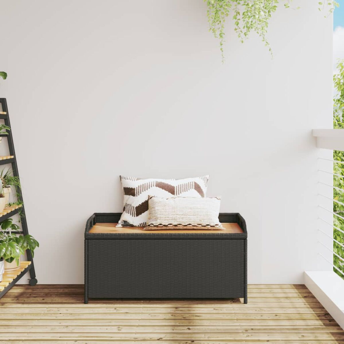 Panca contenitore per esterni con cuscini. Piano marrone, lati neri intrecciati, sfondo muro bianco, piante verdi e terrazza.