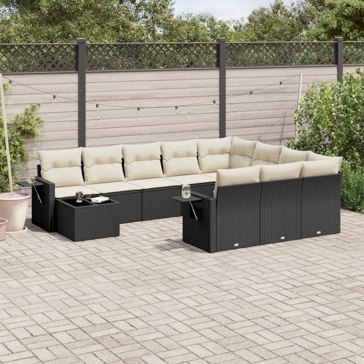 Divano componibile da esterno in rattan nero con cuscini color crema, tavolino, su un patio in mattoni.
