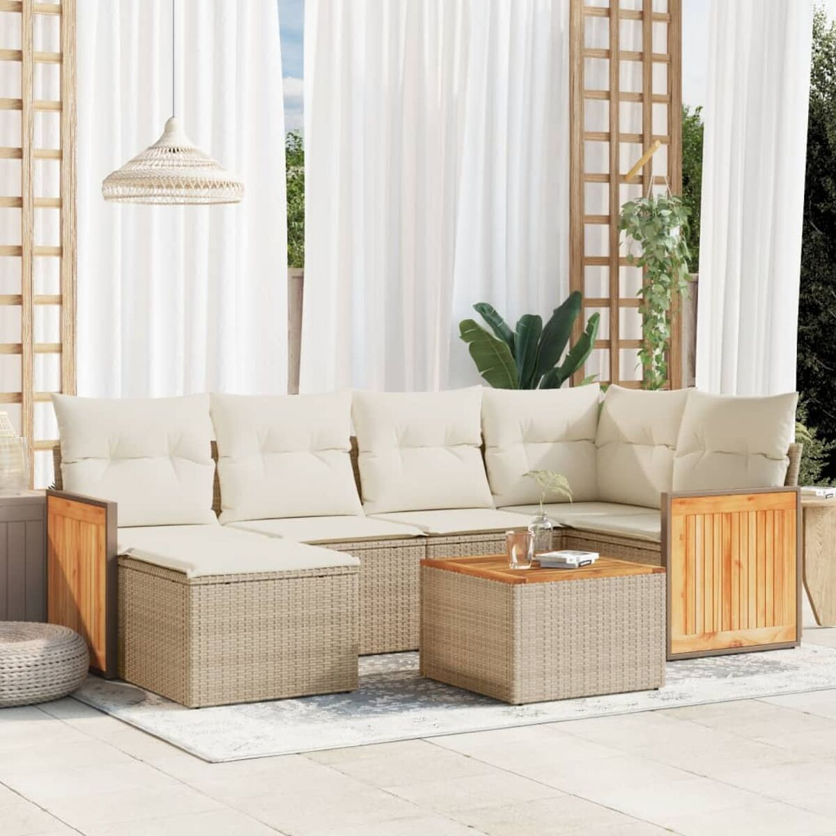 Set divano in vimini da esterno con cuscini color crema, dettagli in legno, tavolino su tappeto bianco.