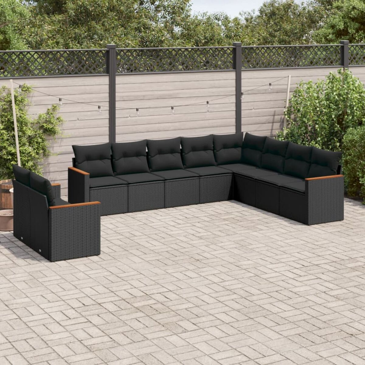 Outdoor-Sofa-Set aus schwarzem Rattan. Es hat Kissen und steht auf einer Ziegelterrasse. Im Hintergrund ein Holzzaun.