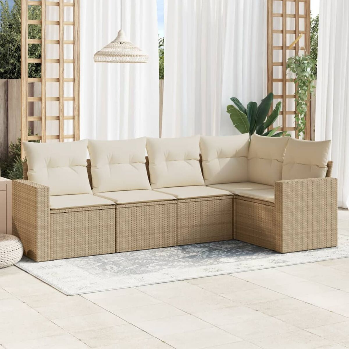 Divano componibile da esterno in vimini con cuscini color crema. Pavimento beige. Tende bianche.