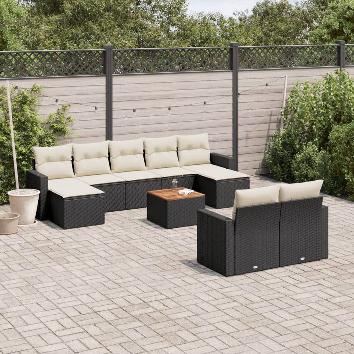 Set di mobili da esterno in vimini nero con cuscini beige su un patio in mattoni.