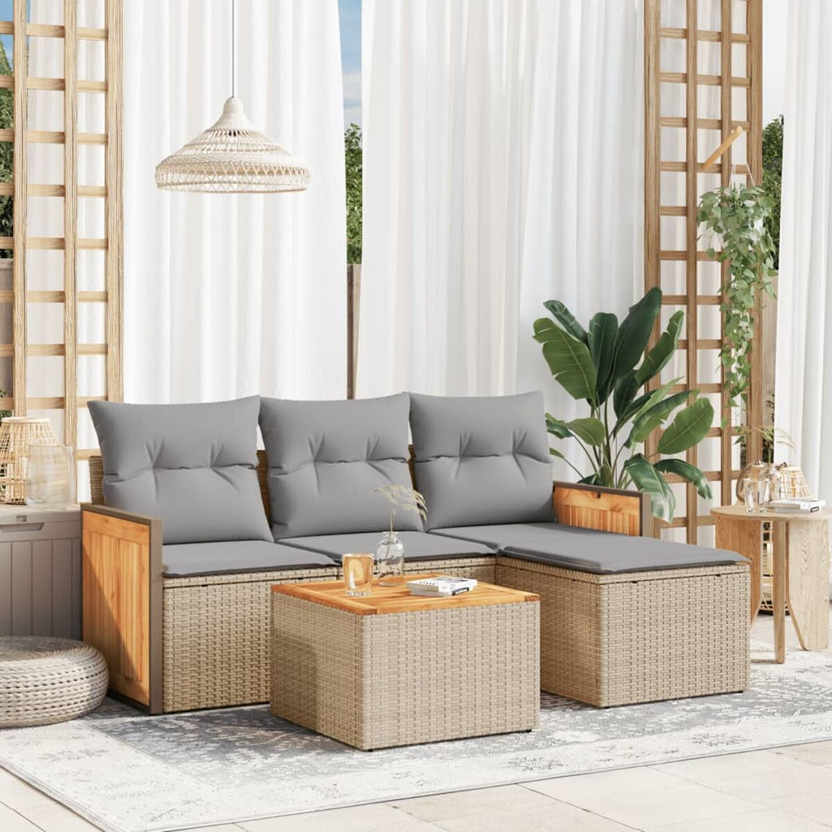 Set da patio con divano intrecciato, cuscini e tavolo in legno. Tende bianche dietro.