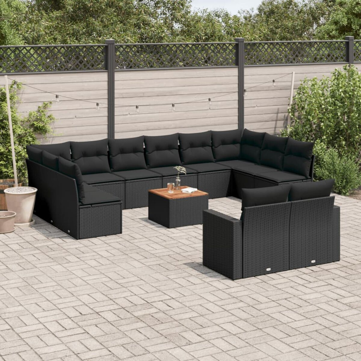 Ein schwarzes Outdoor-Möbelset aus Korbgeflecht, auf einer Steinterrasse angeordnet, mit einem Holztisch und Pflanzen im Hintergrund.