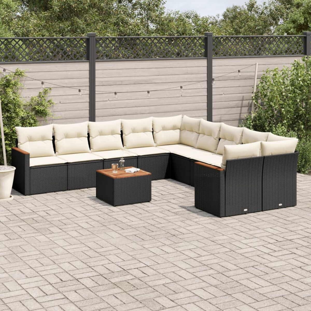 Divano componibile in vimini nero da esterno con cuscini color crema su un patio in mattoni.