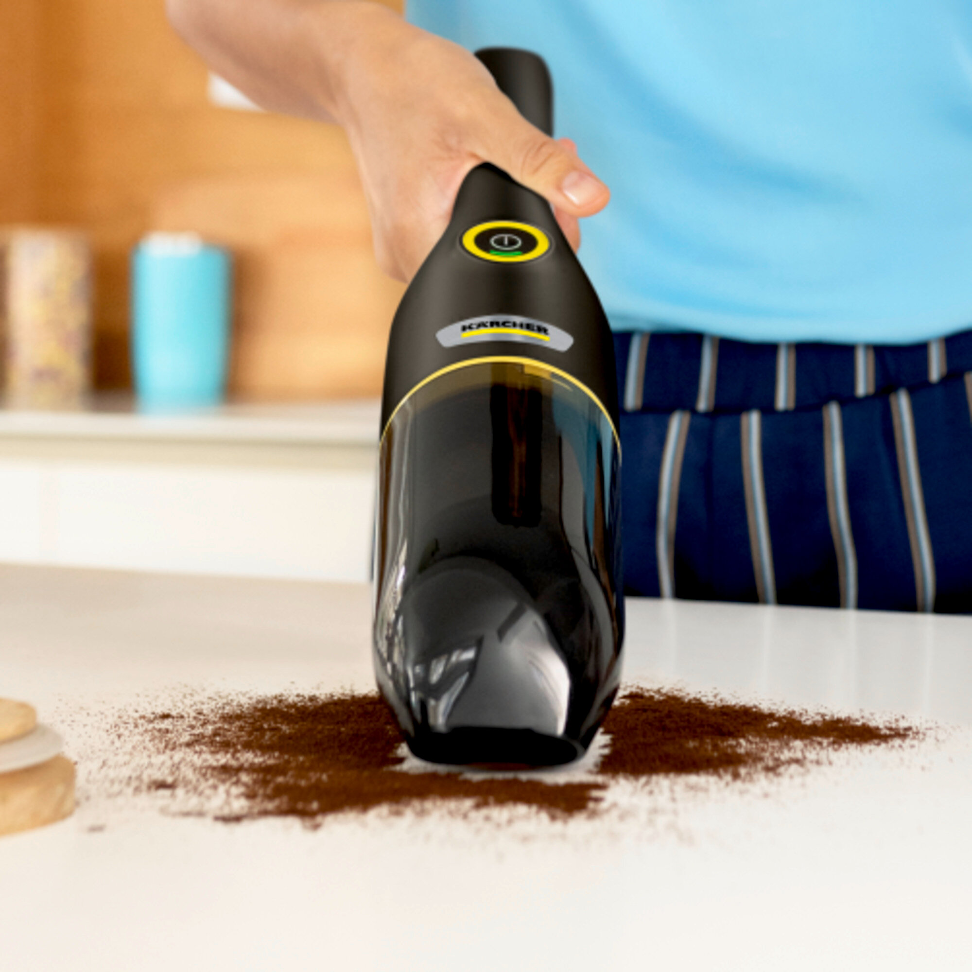 Eine Person benutzt einen schwarzen Staubsauger, um Kaffeepulver auf einer weißen Oberfläche aufzusaugen.